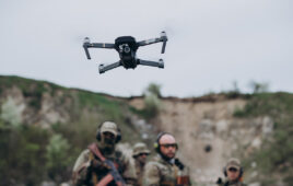 A drone taking off while people in camo watch.